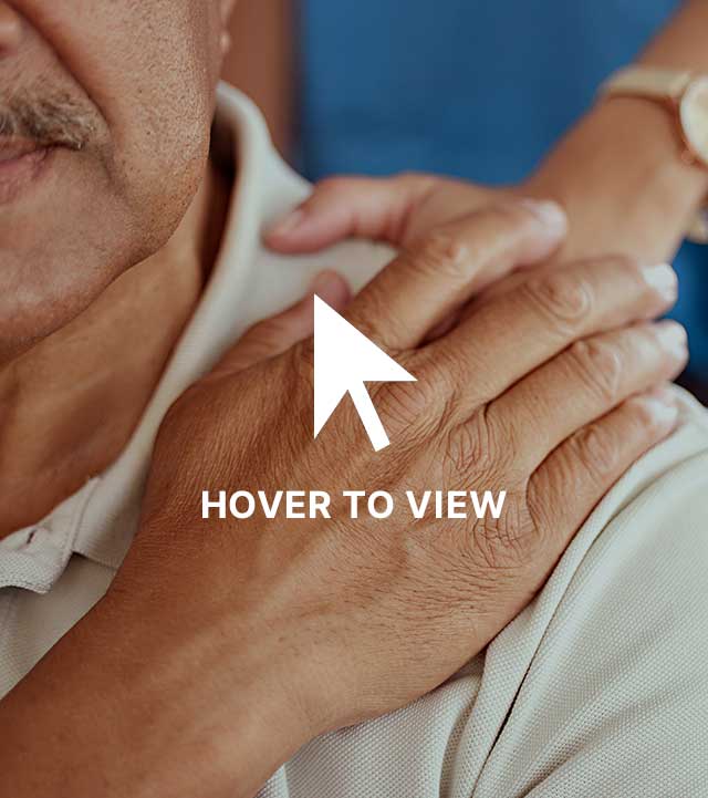 Close-up of an elderly man resting his hand on his chest with a woman's hand gently on his shoulder.