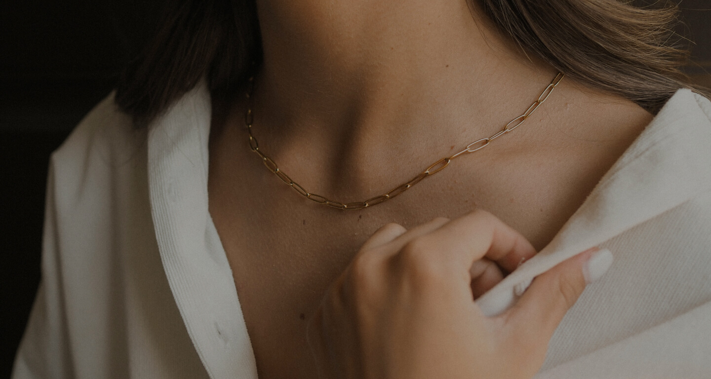 Close-up of a person adjusting the collar of a white shirt, wearing a delicate gold chain necklace.
