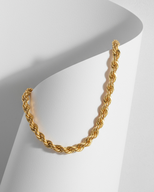 Gold twisted rope chain necklace displayed on curved white backdrop.