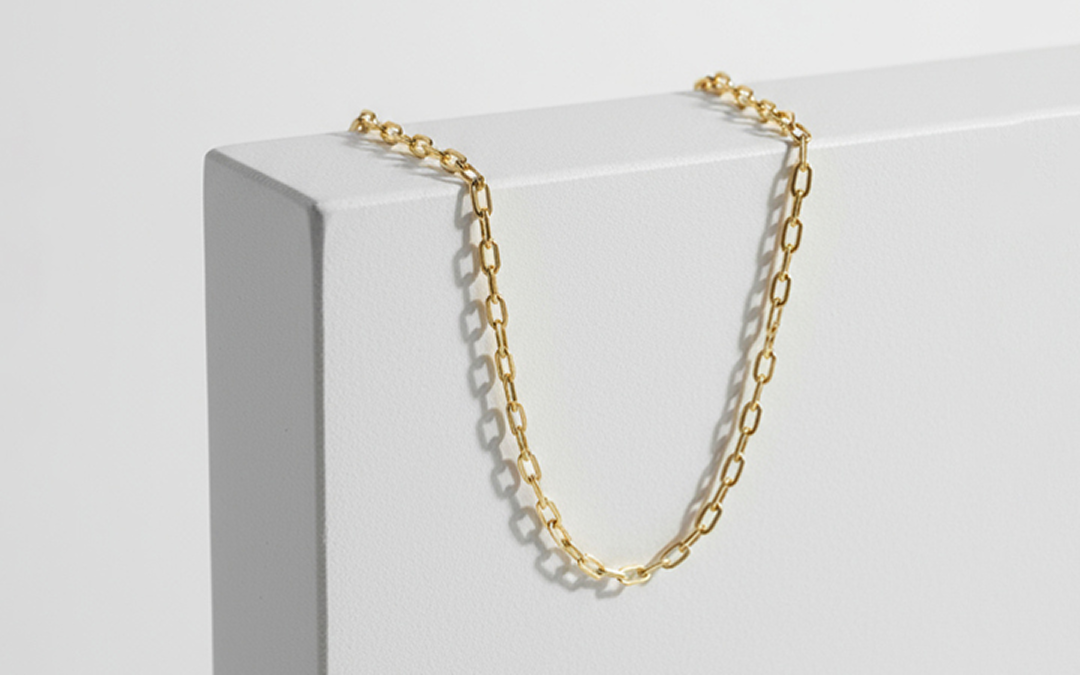 Gold chain necklace draped over the corner of a white textured rectangular block casting a soft shadow.