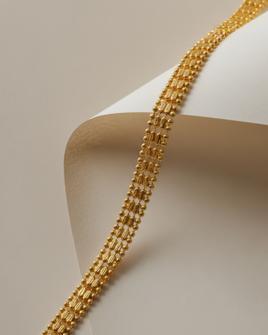 Close-up of a gold ornamental chain with intricate bead and link design draped over curved beige paper.