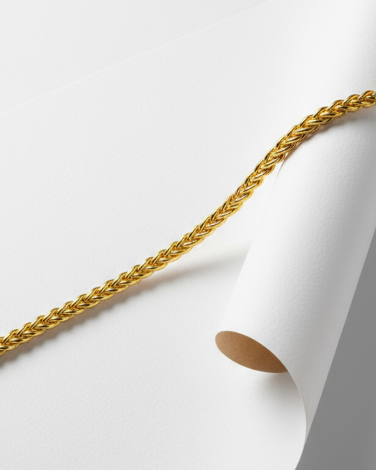 Close-up of a textured gold rope chain resting on a curled white paper surface.