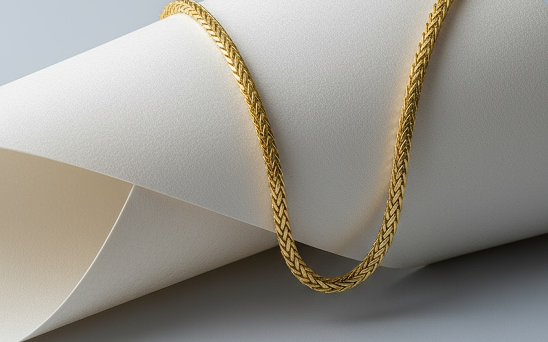 Close-up of a gold braided chain necklace draped over textured white fabric.