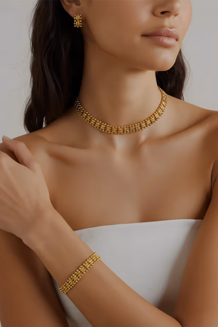 Woman wearing matching gold jewelry set including a choker necklace, bracelet, and earrings, dressed in a white strapless top.