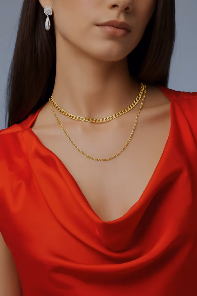 Close-up of a woman wearing a red satin top, layered gold necklaces, and a silver teardrop earring with small stones.