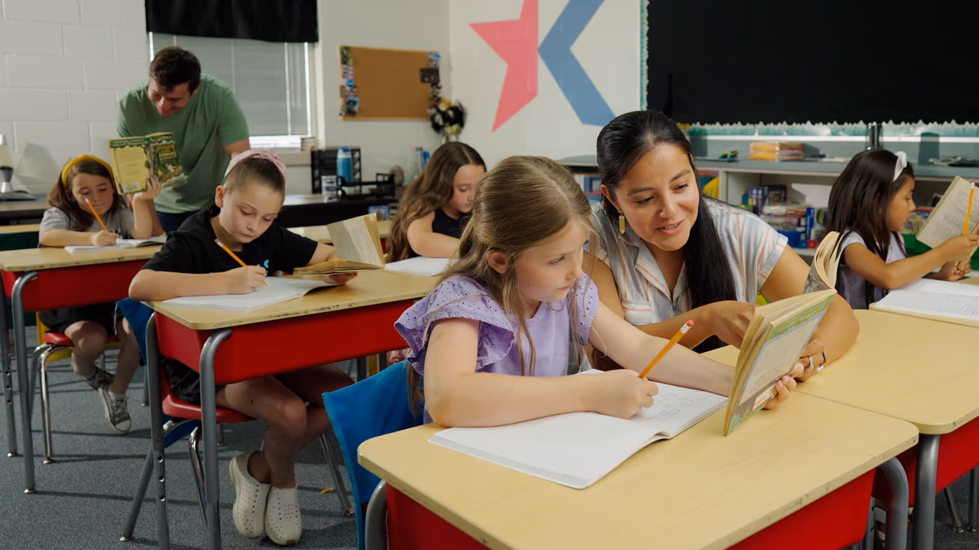 A happy female Teacher helping a student with her work at a desk.