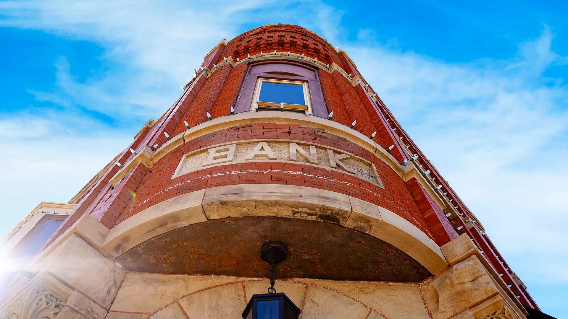 Photo of the front of a old corner bank building with blue skys and white clouds.