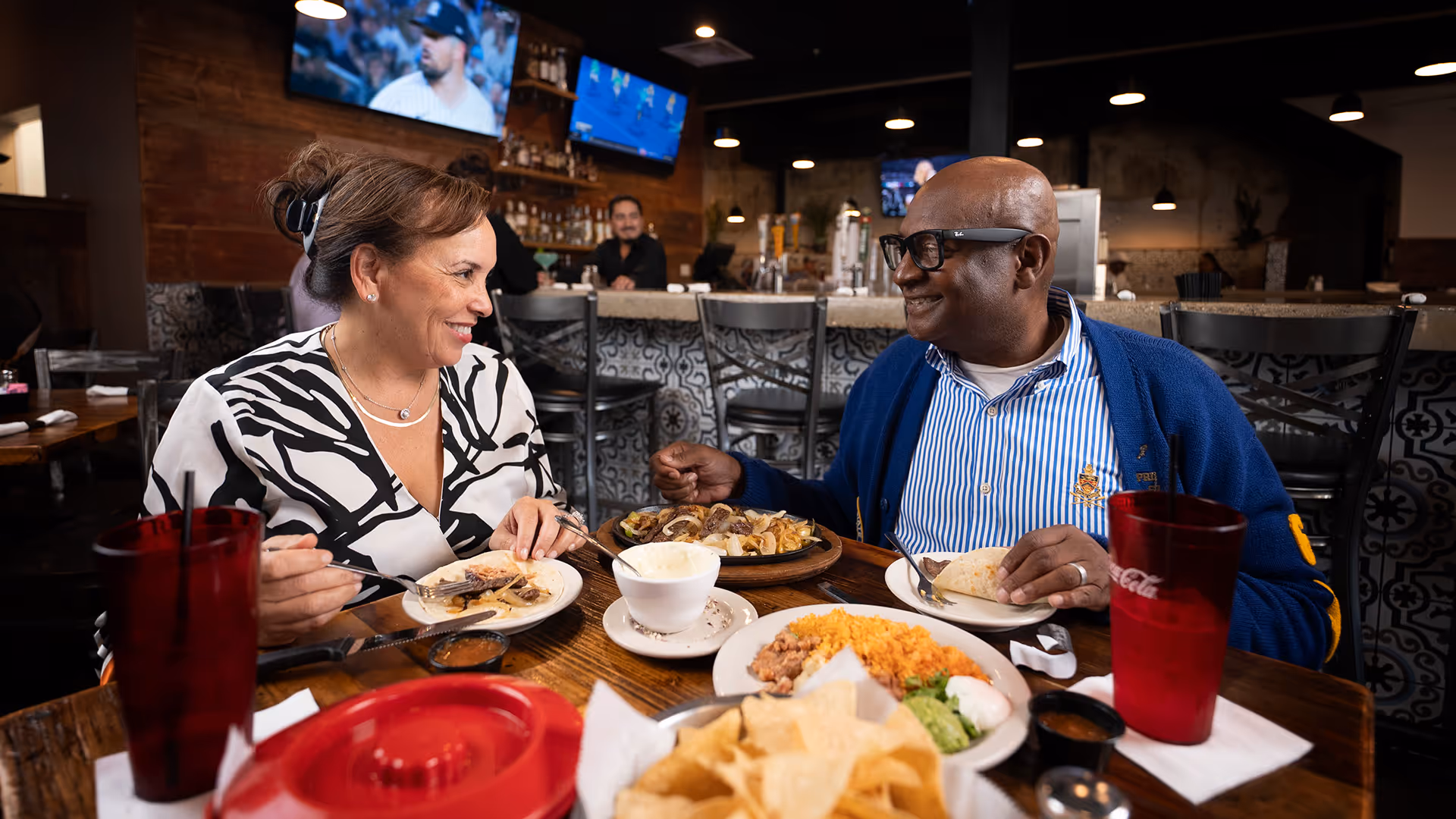 Smiling man and woman enjoying a meal together at a restaurant table with Mexican dishes and drinks.