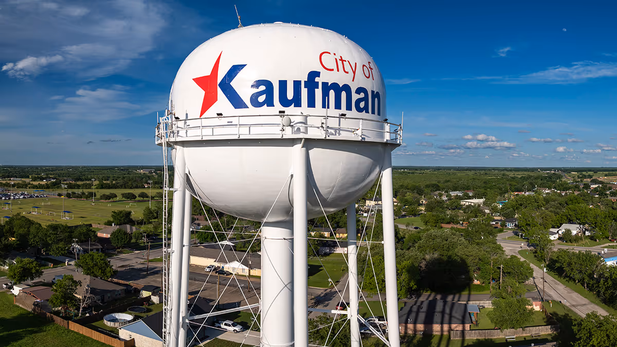 White water tower with red star and blue text reading 'City of Kaufman' under a blue sky with scattered clouds.