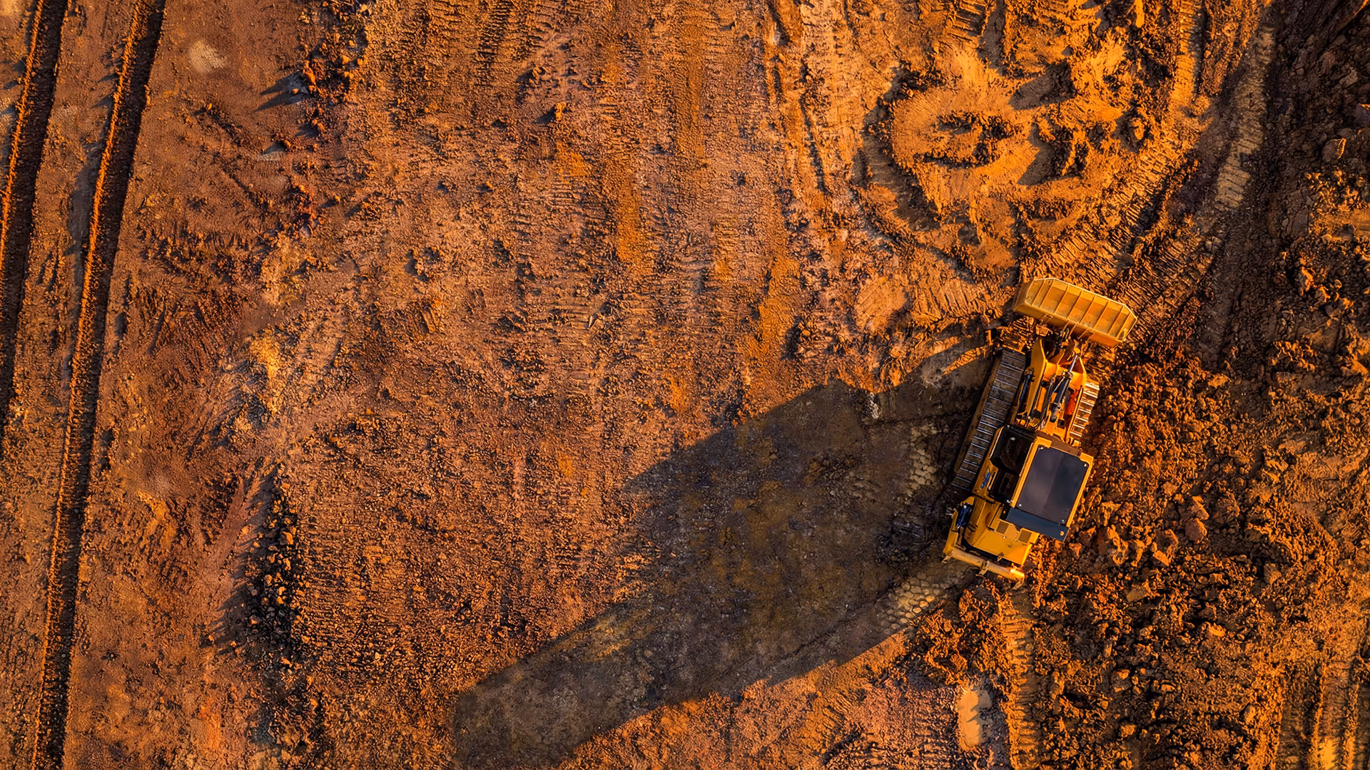 Aerial view of a yellow bulldozer working on reddish dirt at a construction site.