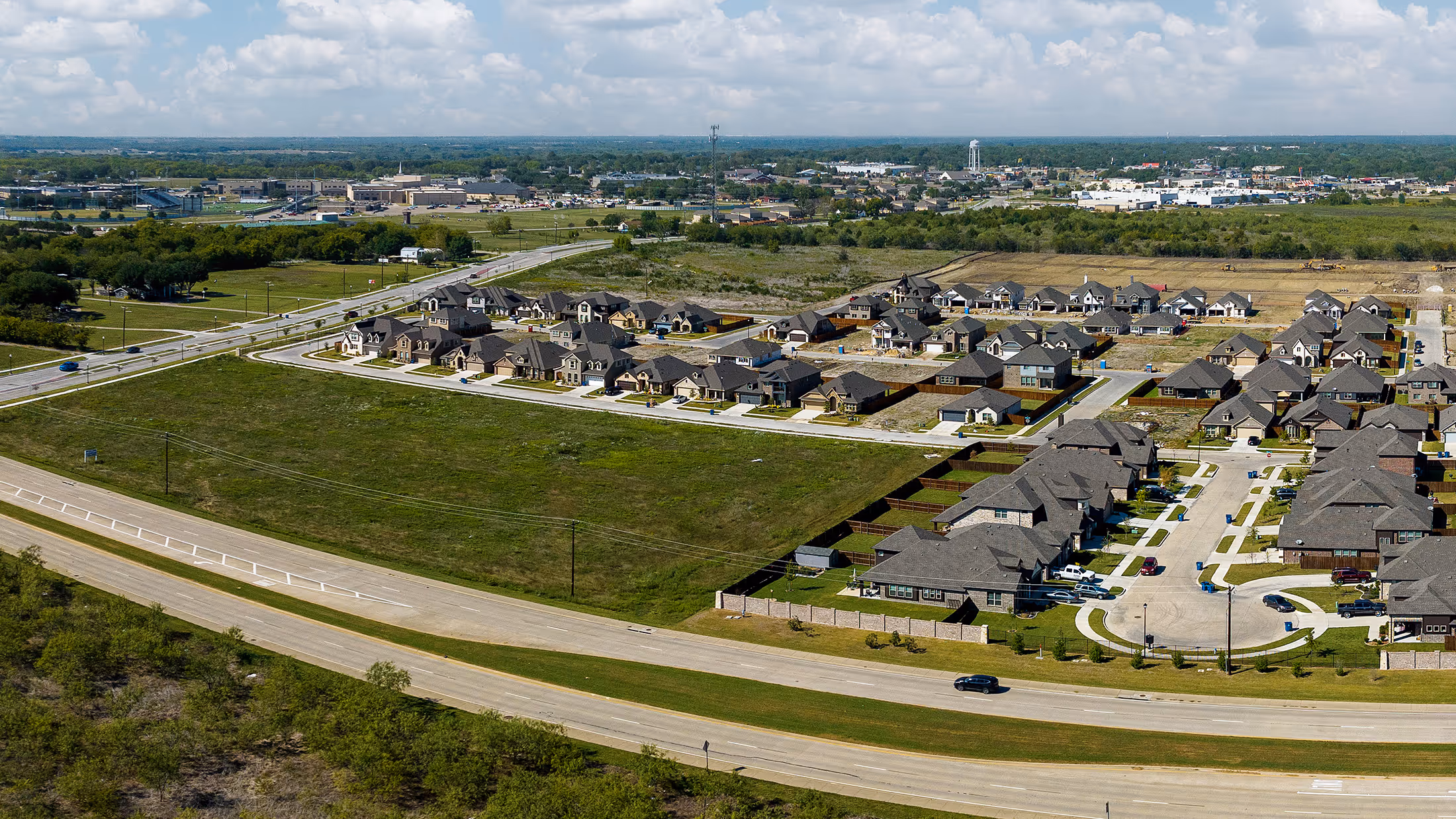 Aerial view of a suburban neighborhood with single-family homes and green open fields around roads.