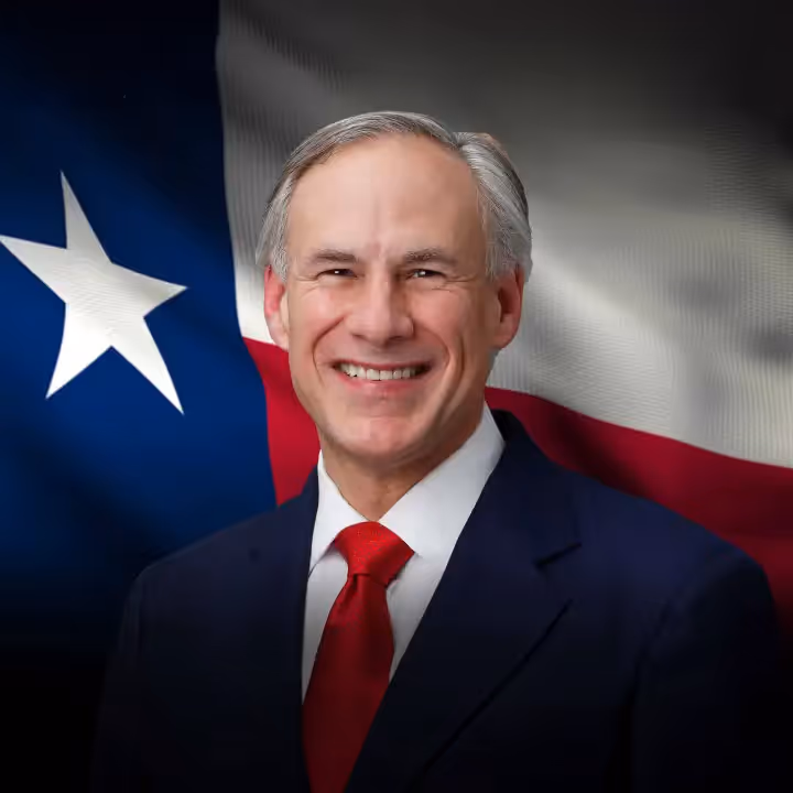 Smiling man in suit and red tie in front of a waving Texas state flag.