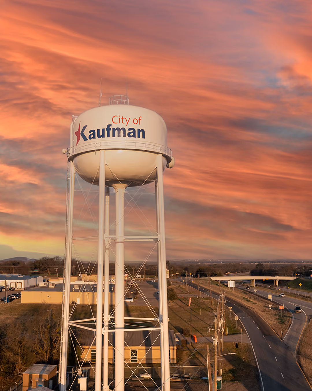 City of Kaufman white water tower with a sunset sky and highway in the background.