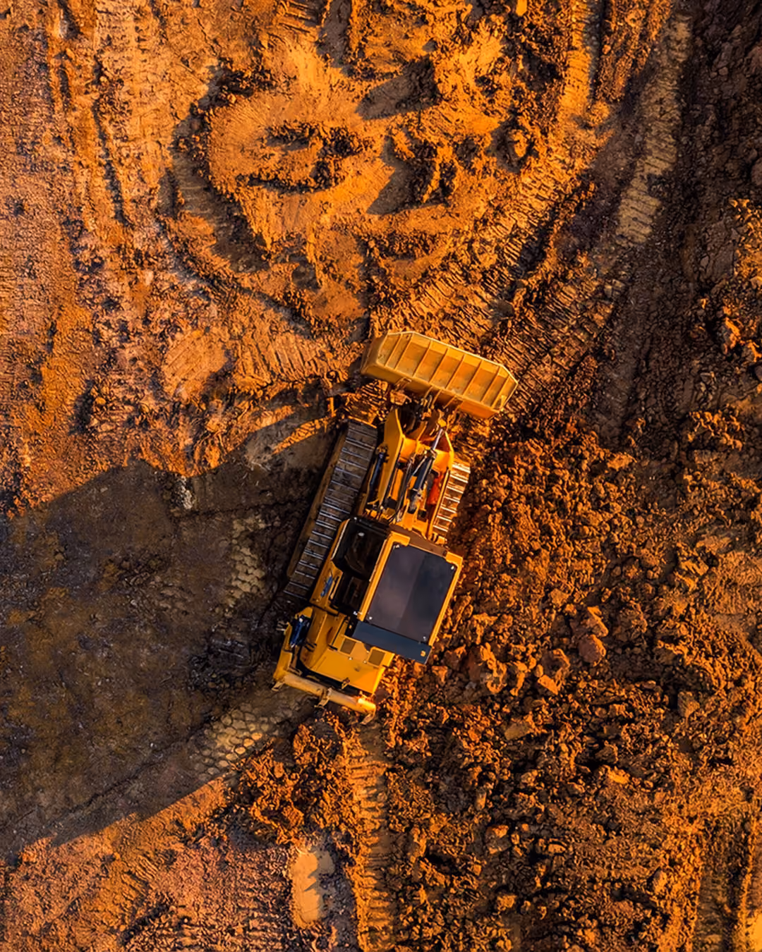 Aerial view of a yellow bulldozer moving dirt on a construction site with tire tracks visible.