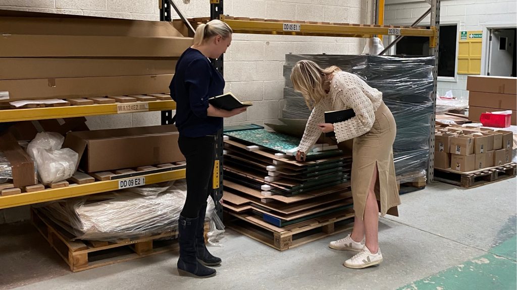 Two Ripple team members inspecting finished retail fixtures stacked on pallets inside the company’s warehouse.