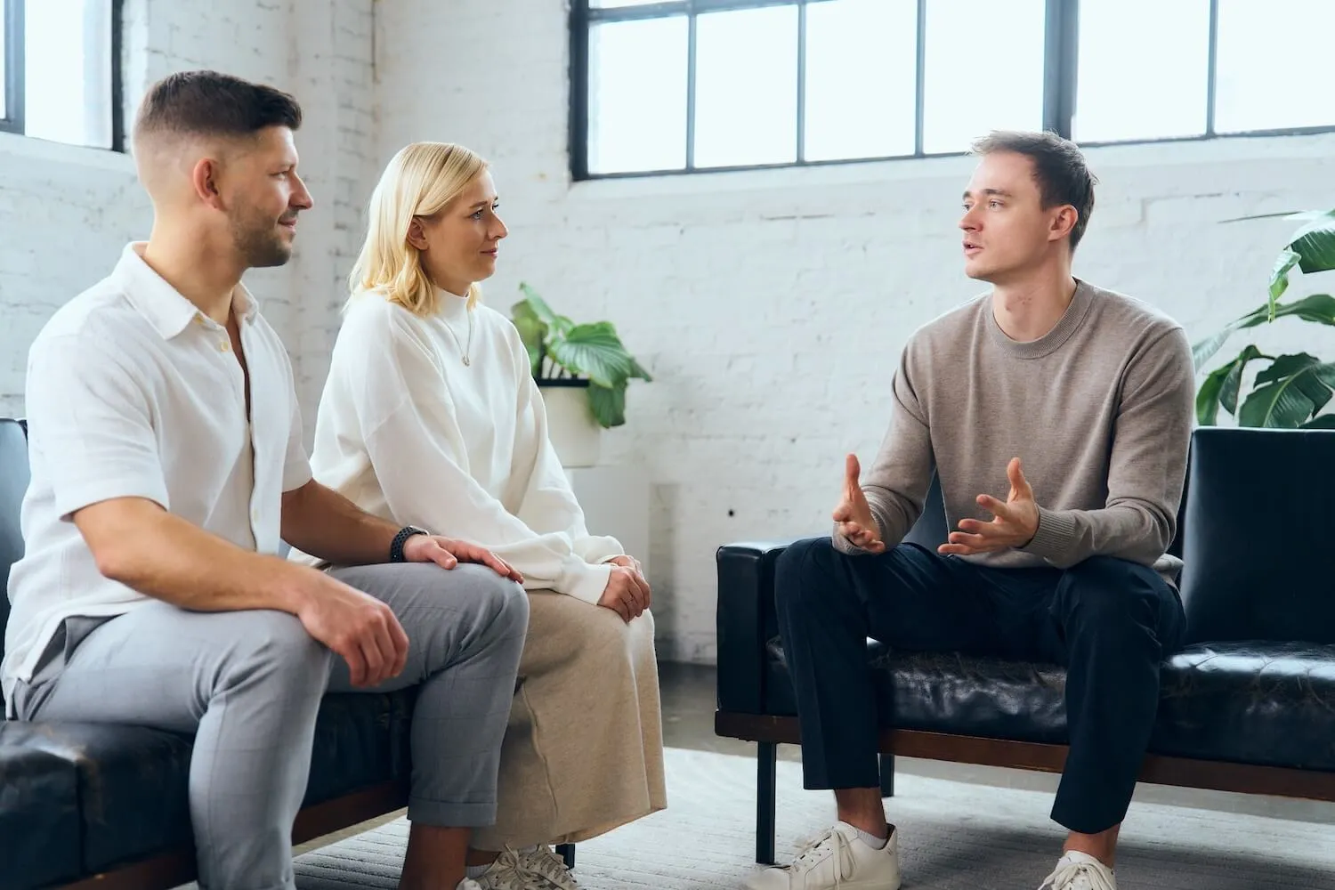 Three people sitting on sofas in a bright room having a serious conversation.