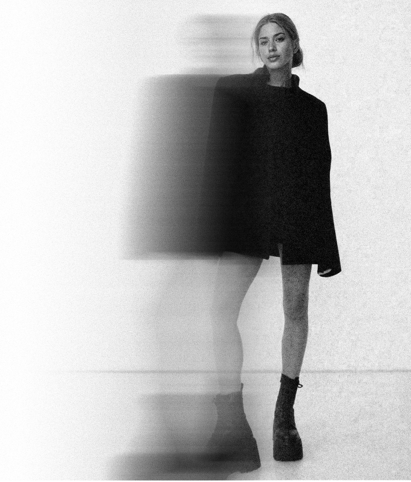 Black and white photo of a woman in a black oversized sweater and platform boots with a motion blur effect on her left side.