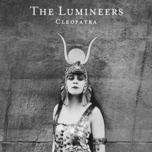 Black and white photo of a woman in a decorative outfit and headpiece with horns, styled like Cleopatra against a plain textured wall; album title and band name above her.
