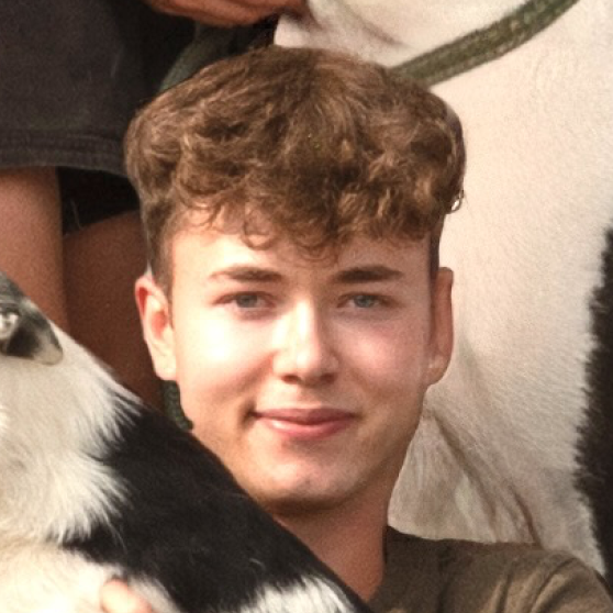 Young man with curly brown hair smiling, holding a black and white dog.