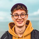 Young man wearing yellow hoodie and glasses smiling with ocean and sky background