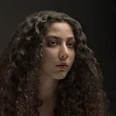 Woman with long curly dark hair and neutral expression against dark background