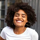 Woman with curly dark hair smiling wearing white t-shirt and hoop earrings