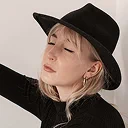 Woman wearing black cowboy hat and black jacket with minimal background