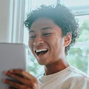 Young man with curly dark hair smiling while holding tablet device indoors
