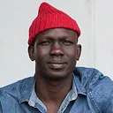 Man with dark skin wearing red beanie and blue denim shirt against white background