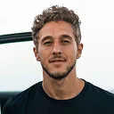 Man with curly brown hair wearing black shirt against white background