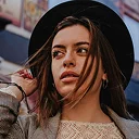 Young woman with long hair wearing a black hat and looking away outdoors.