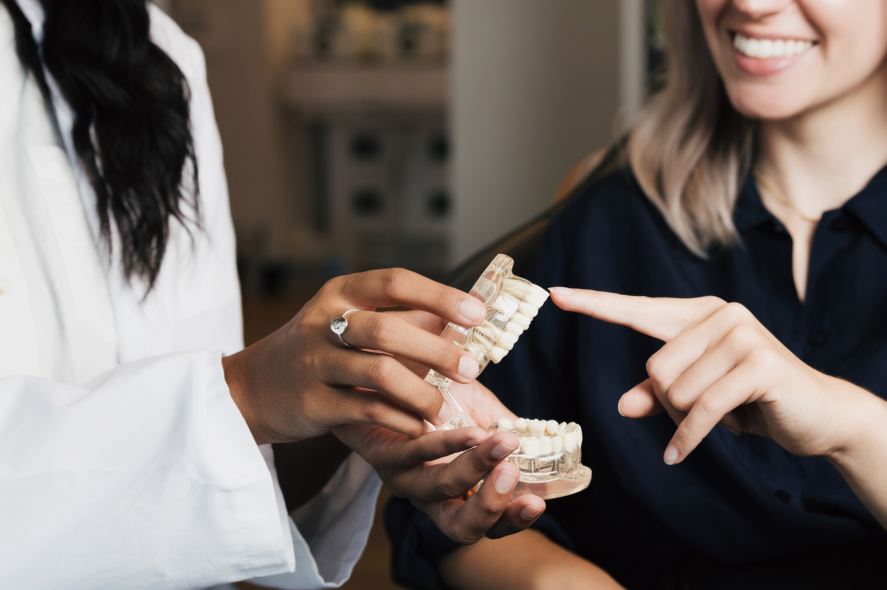 A dental professional holding a teeth model while a smiling patient points at the upper teeth.