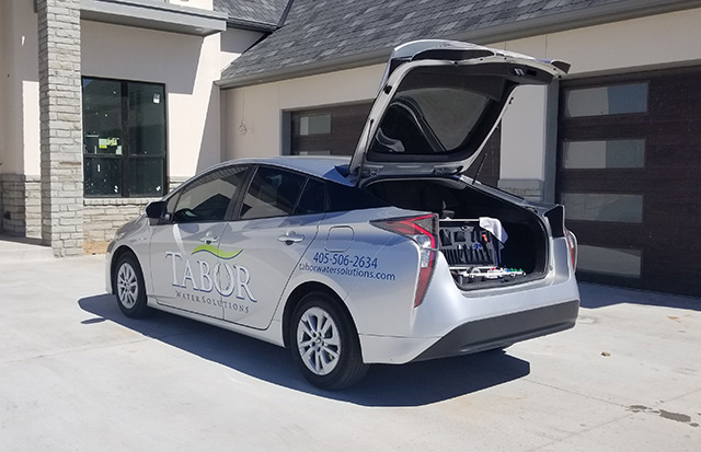 Silver Tabor Water Solutions car parked with rear hatch open showing water testing equipment inside.
