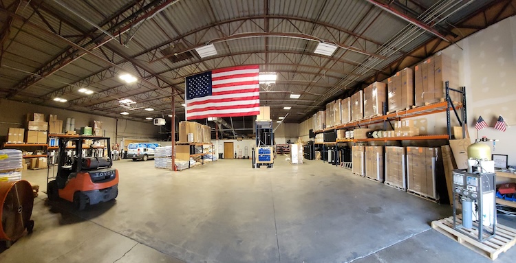 Wide view of a warehouse interior with shelves stocked with boxes and an American flag hanging from the ceiling