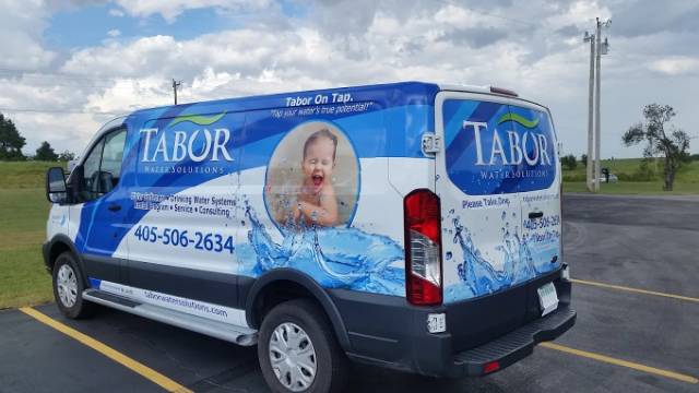 Van with blue and white Tabor Water Solutions advertising wrap featuring a child playing in water, company phone number, and website.