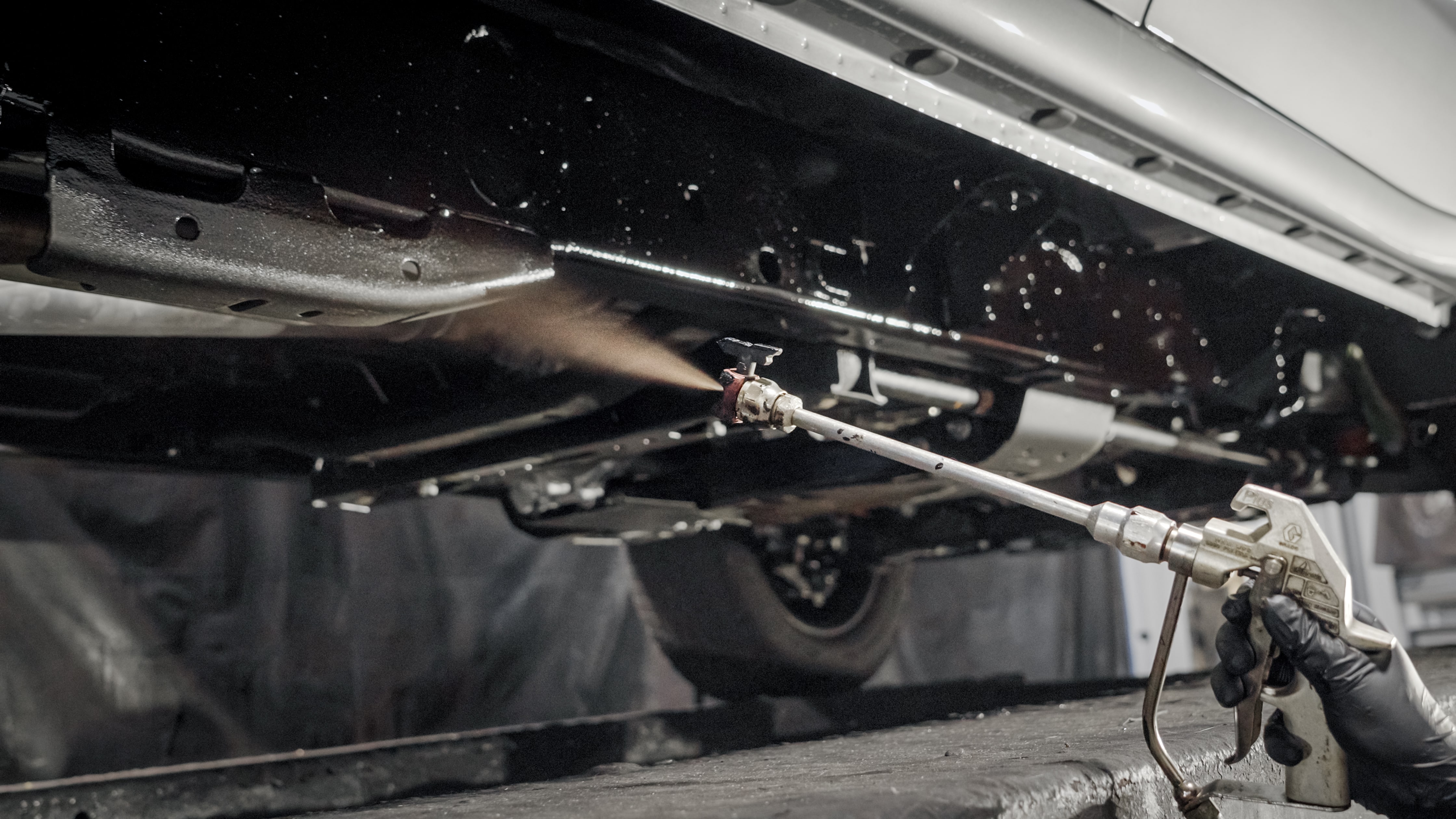 Vehicle frame being treated with professional rustproofing spray by Madison Auto Trim, Wisconsin. Vehicle corrosion protection, anti-rust undercoating, and preventive rustproof services.