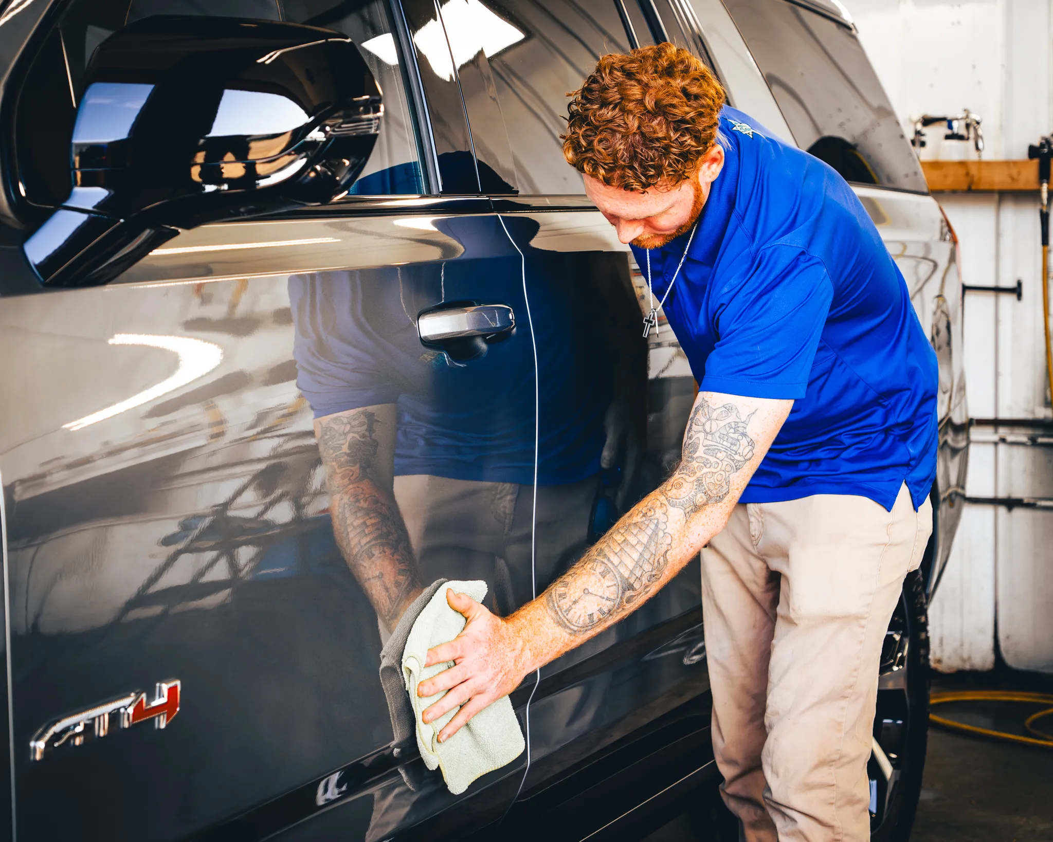 Photo of a man in a blue shirt and khakis with forearm tattoos wiping down and polishing a GMC Sierra AT4 after a full-service exterior and interior auto detail from Madison Auto Trim, LLC