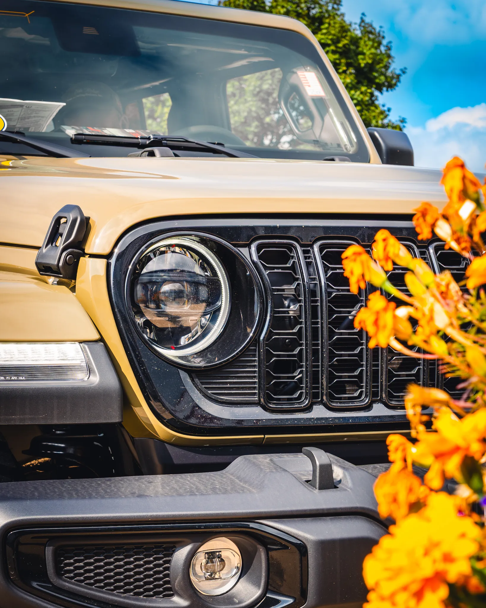 Photo of a yellow Jeep Gladiator in front of yellow summer flowers right after a finished custom Katzkin leather interior upgrade from Madison Auto Trim, LLC.