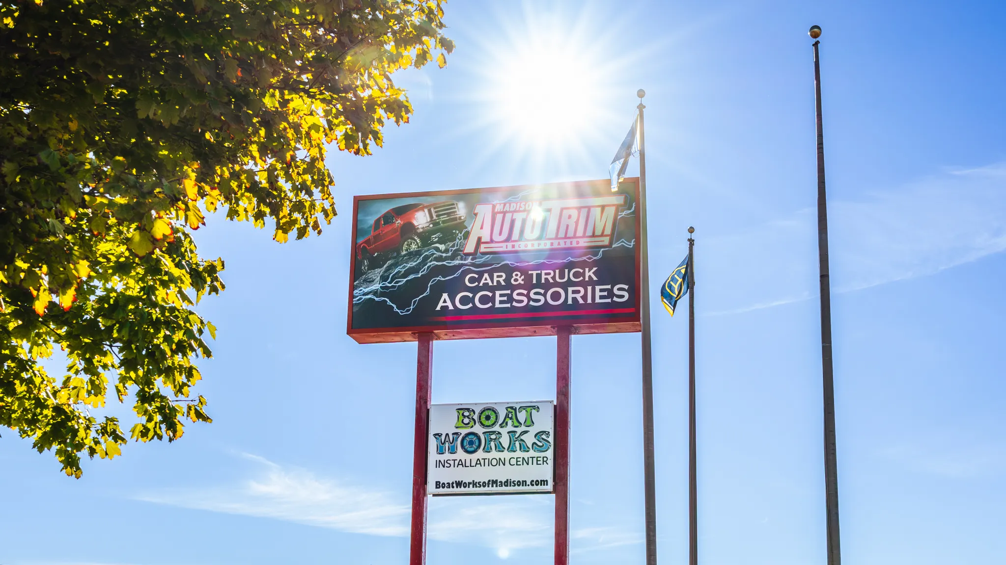 Photo of the outside signage surrounding Madison Auto Trim and Boat Works of Madison, Wisconsin. Sun flares peering over the top of the structure that reads "Car & Truck Accessories" and "Boat Works Installation Center"