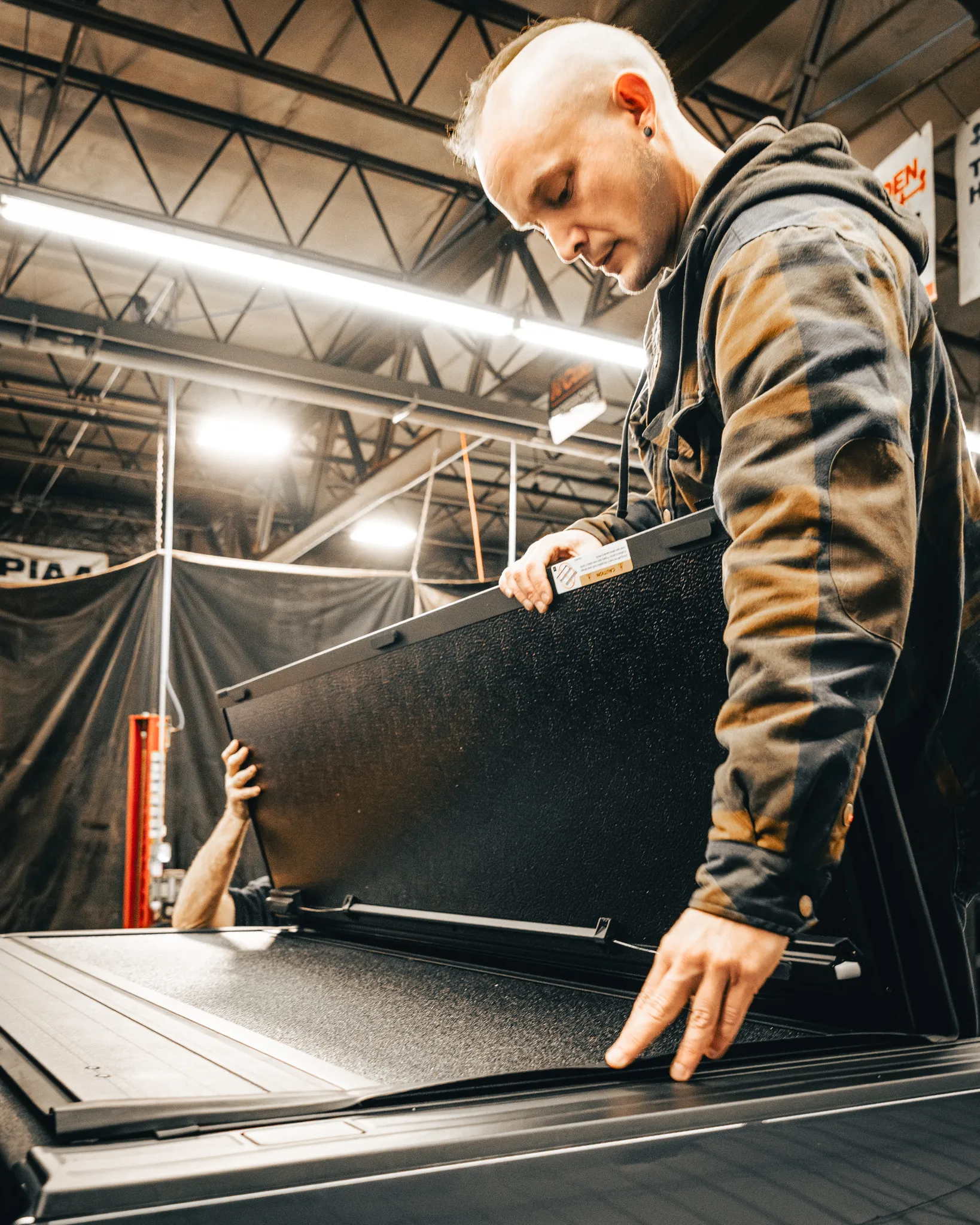 A man in a large flannel jacket working on a Tonneau Cover installation with another worker at Madison Auto Trim, LLC.