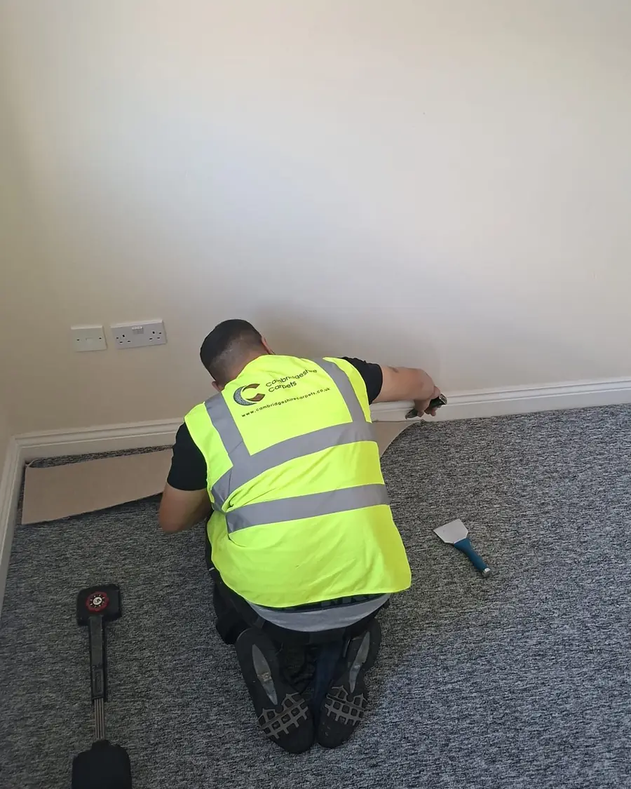 A Cambridgeshire Carpets fitter in branded hi-vis fitting grey carpet
