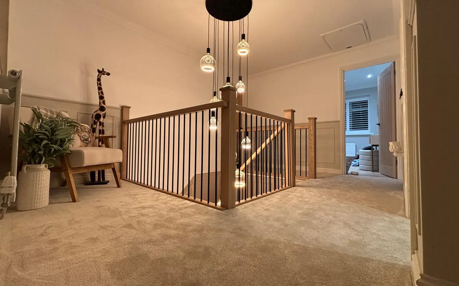 Newly fitted neutral carpet on a landing and staircase in a Cambridgeshire home, with oak balustrade and pendant lighting