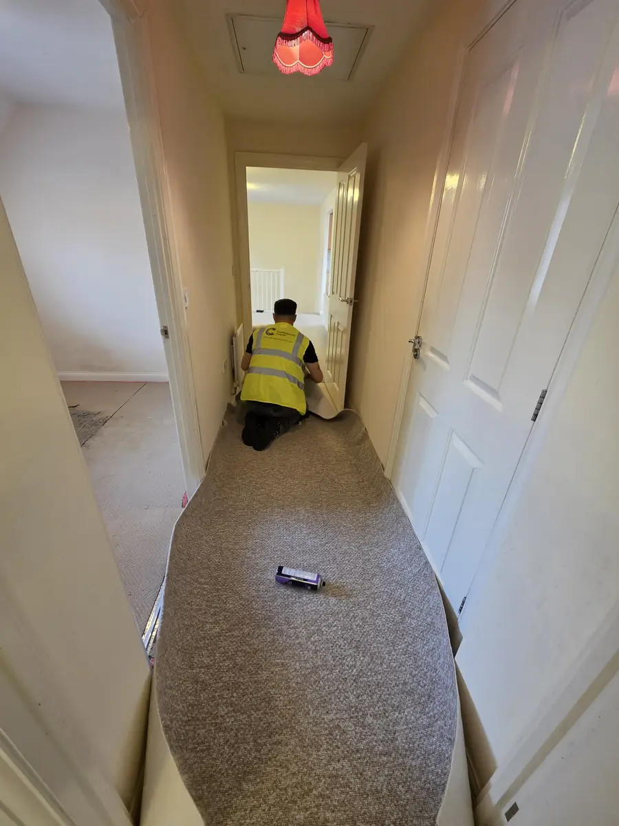 A Cambridgeshire Carpets fitter laying carpet along a hallway