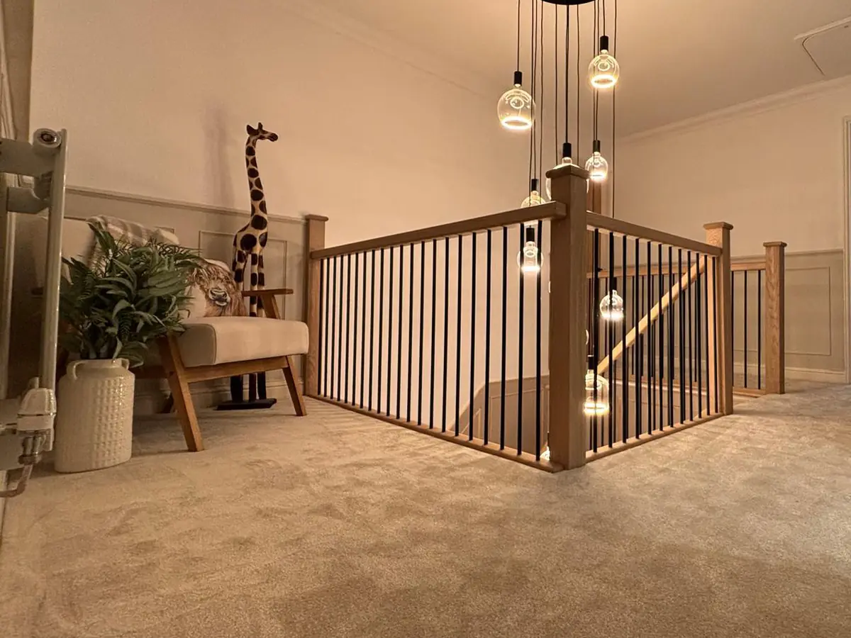 Finished landing in a Hampton new build: neutral carpet, oak and black metal balustrade and a cluster of pendant lights