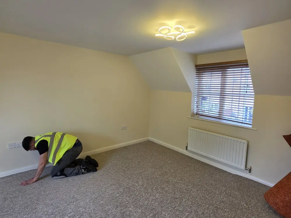 A Cambridgeshire Carpets fitter in hi-vis fitting grey twist carpet in a loft bedroom