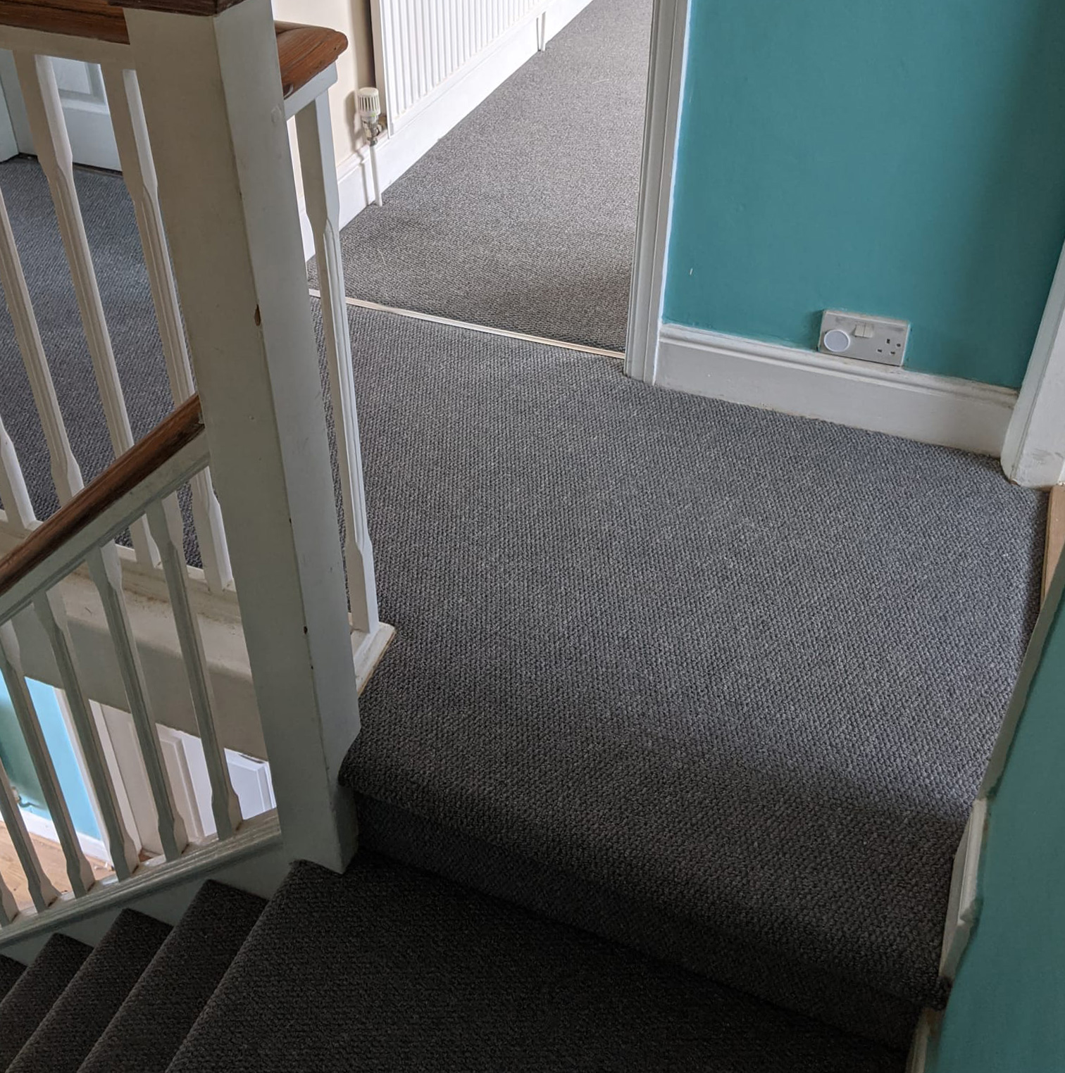 Grey carpeted staircase and landing with white wooden railing and teal walls.