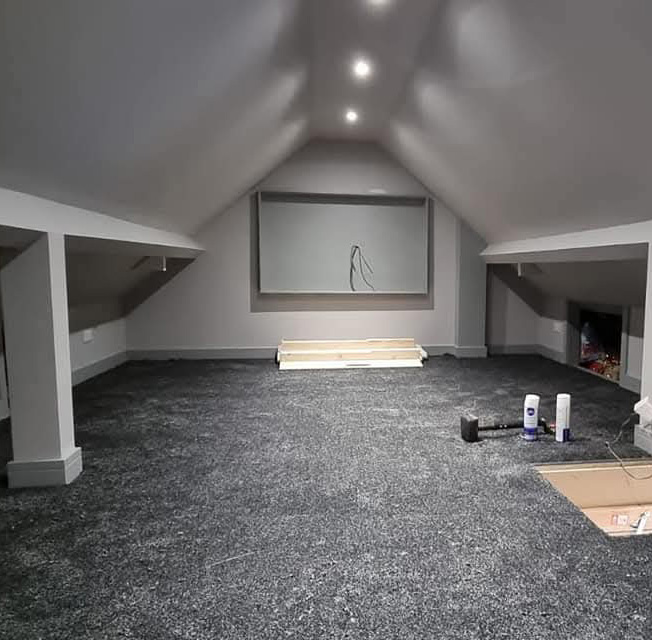 Spacious attic room with sloped ceilings, newly installed dark gray carpet, and recessed ceiling lights.