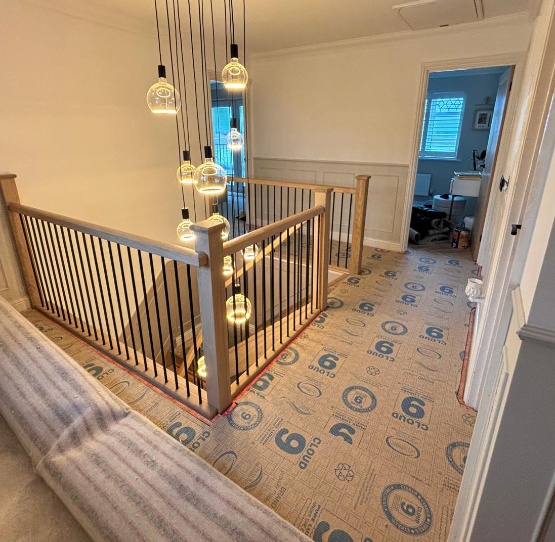 Staircase landing with temporary protective floor covering labeled Cloud 9, modern hanging glass pendant lights, and a partially open door to a room with white walls and window blinds.