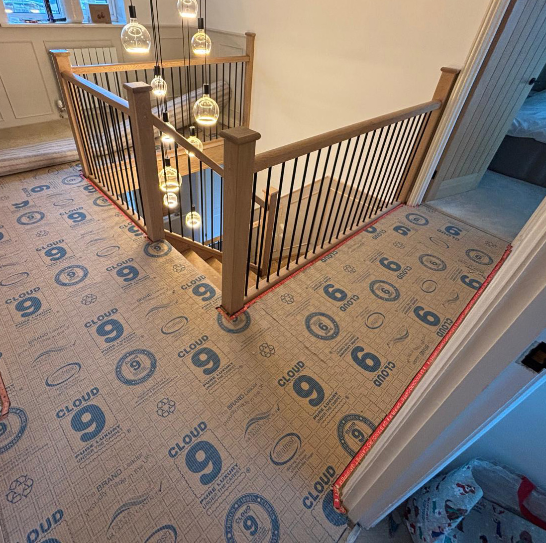 Indoor stairwell with wooden handrails and black vertical balusters, surrounded by protective carpet covering labeled 'Cloud 9'.