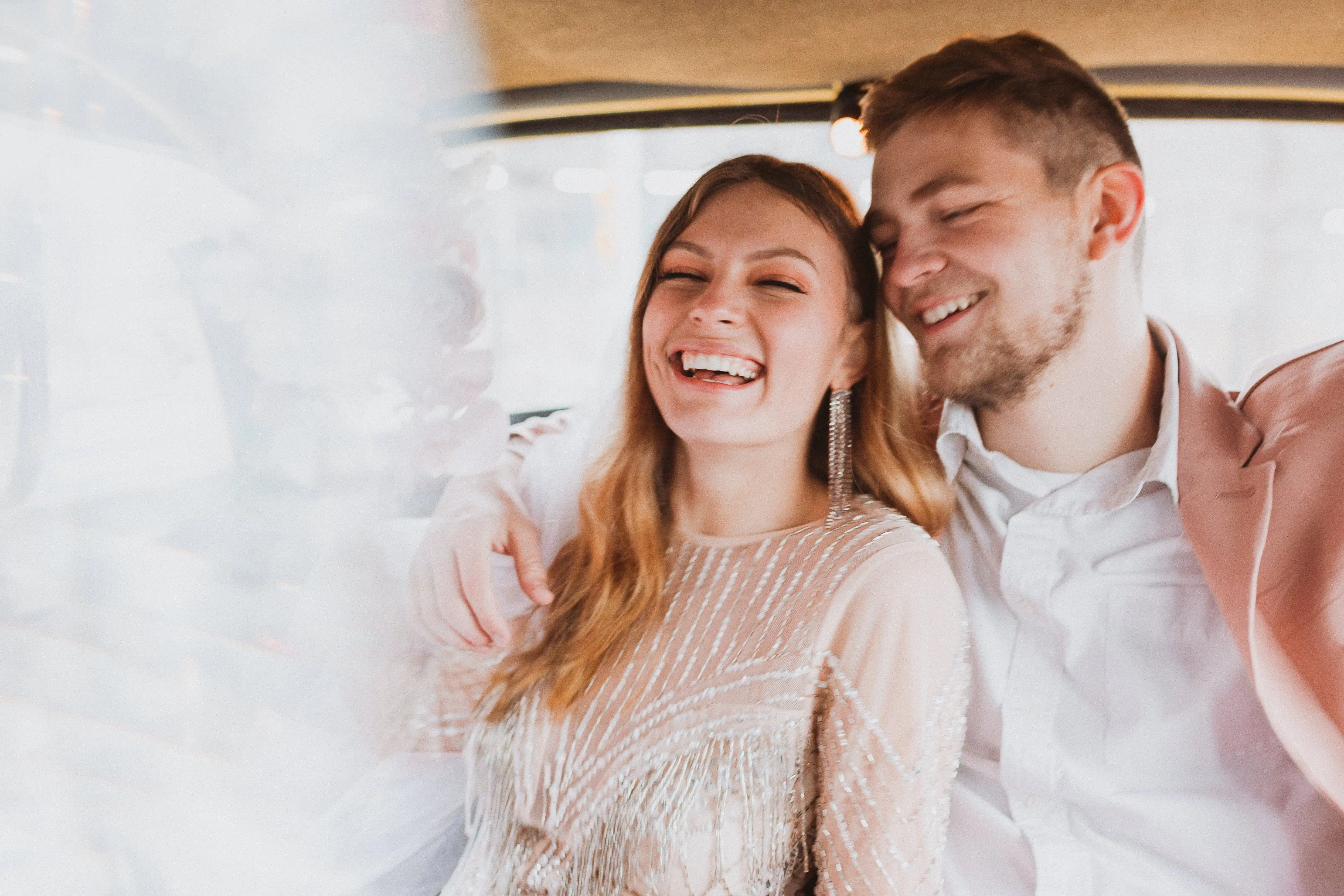 Smiling couple dressed in formal attire sitting close together, enjoying a joyful moment.